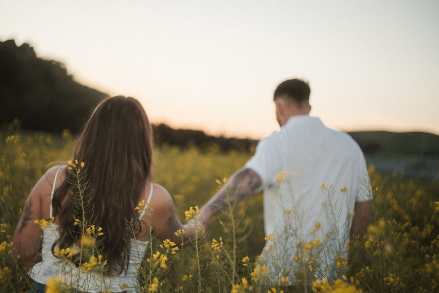 Couple walking through yellow wildflowers at golden hour